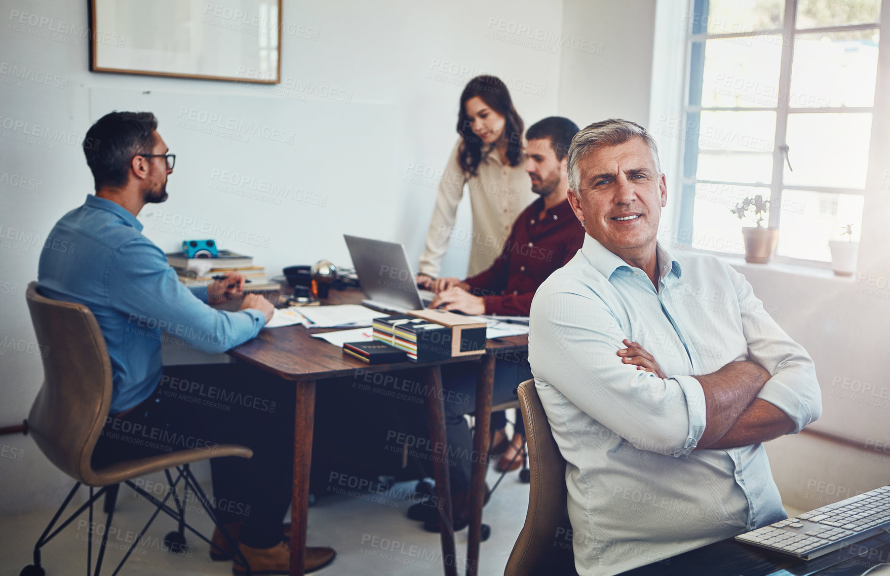 Buy stock photo Portrait of a mature man working in the office with his colleagues in the background