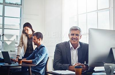 Buy stock photo Portrait of mature businessman using a computer at work with his colleagues in the background