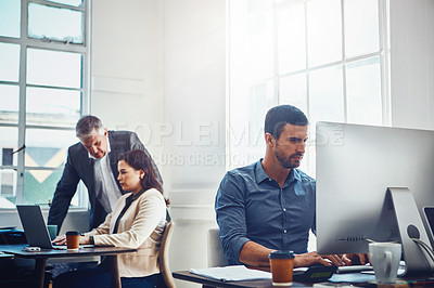 Buy stock photo Shot of young businessman using a computer at work with his colleagues in the background