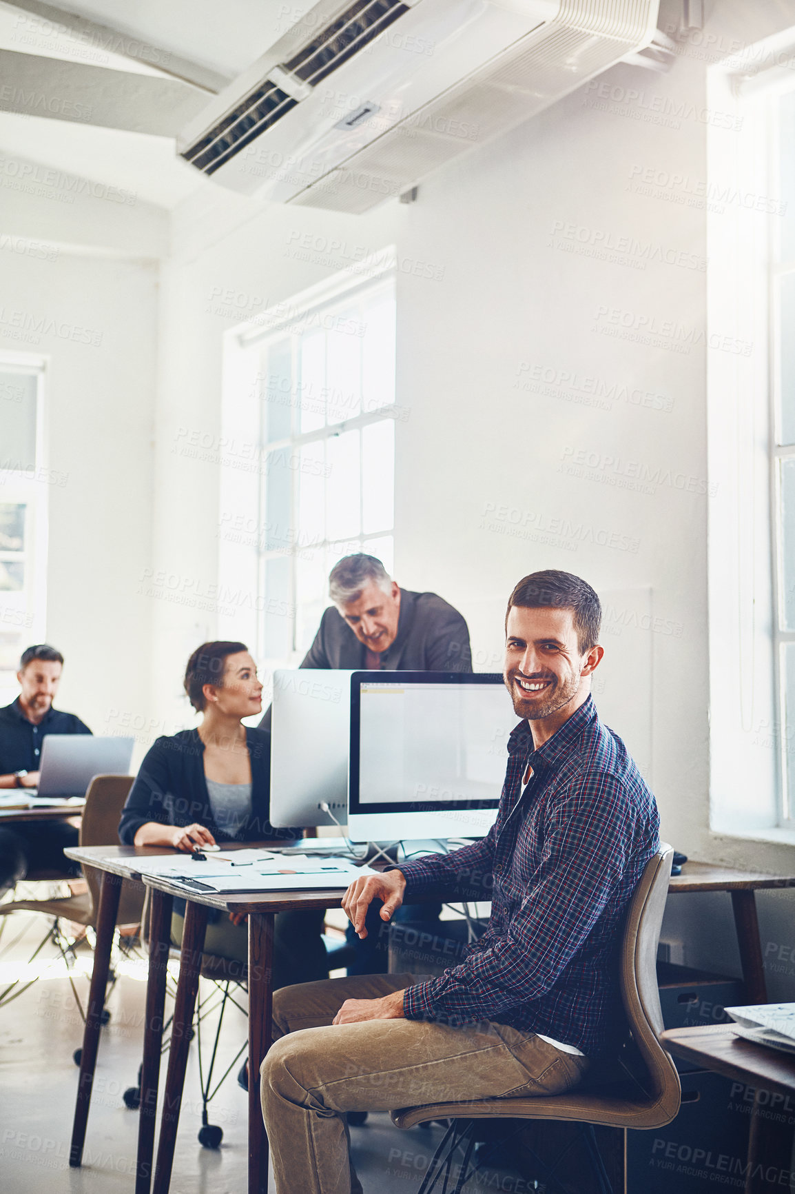 Buy stock photo Portrait of young businessman using a computer at work with his colleagues in the background