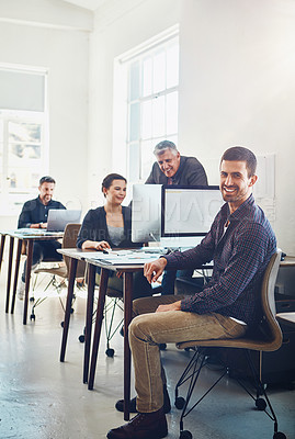 Buy stock photo Portrait of young businessman using a computer at work with his colleagues in the background