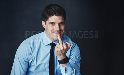 Buy stock photo Studio portrait of a young businessman showing the middle finger against a dark background