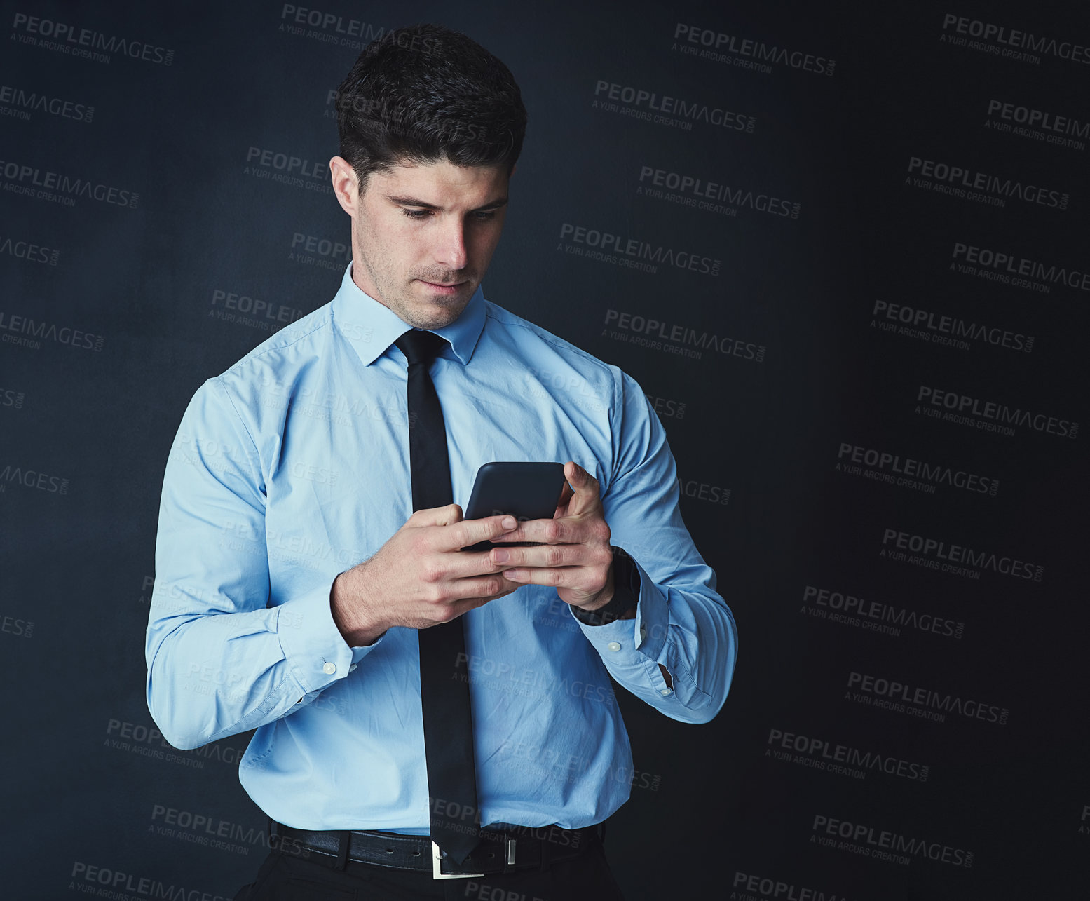 Buy stock photo Studio shot of a young businessman texting on a cellphone against a dark background