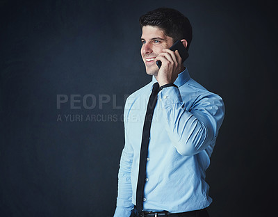 Buy stock photo Studio shot of a young businessman talking on a cellphone against a dark background