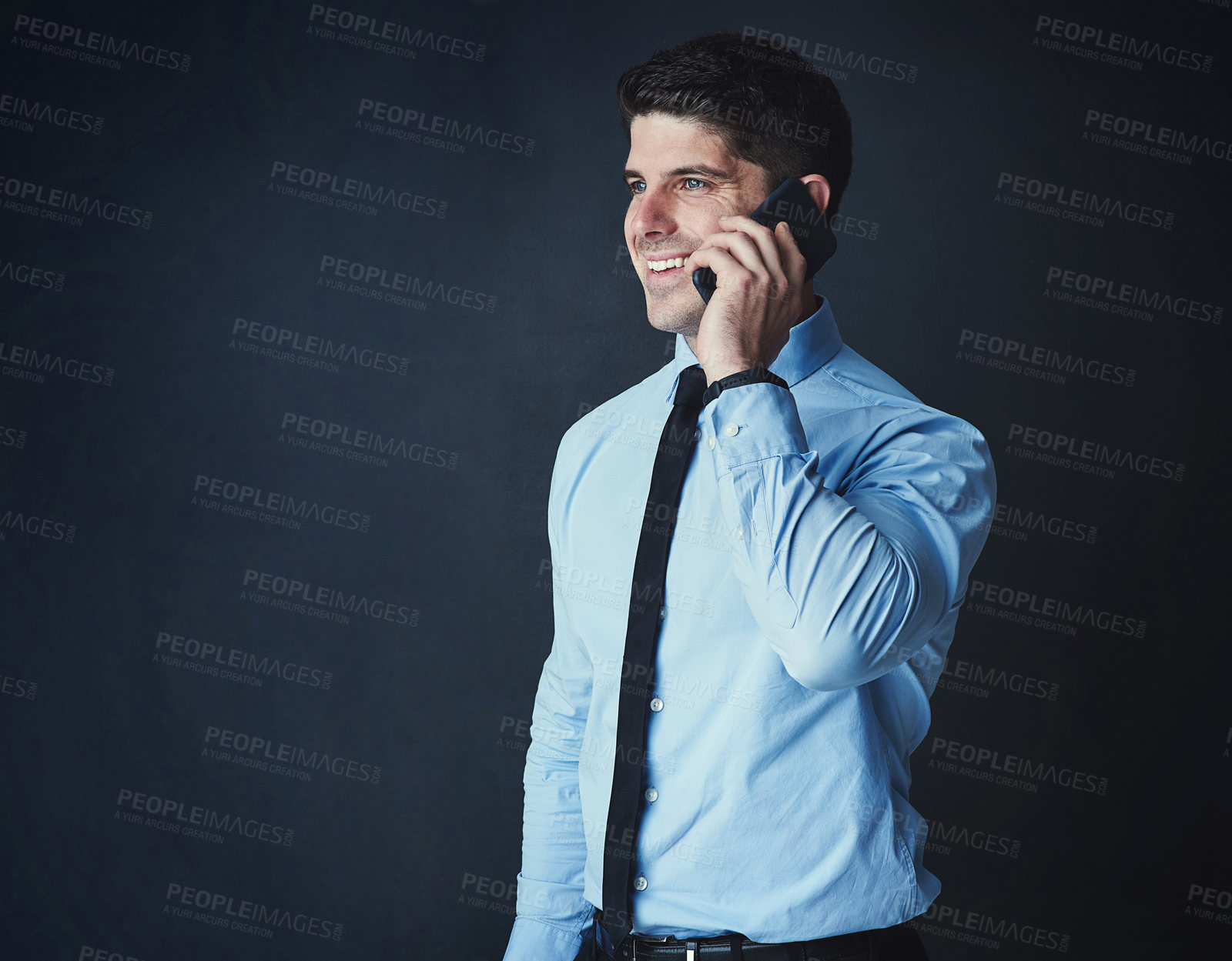 Buy stock photo Studio shot of a young businessman talking on a cellphone against a dark background