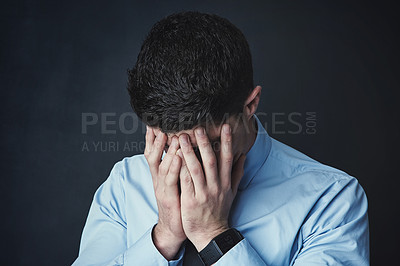 Buy stock photo Studio shot of a young businessman with his hands covering his face against a dark background