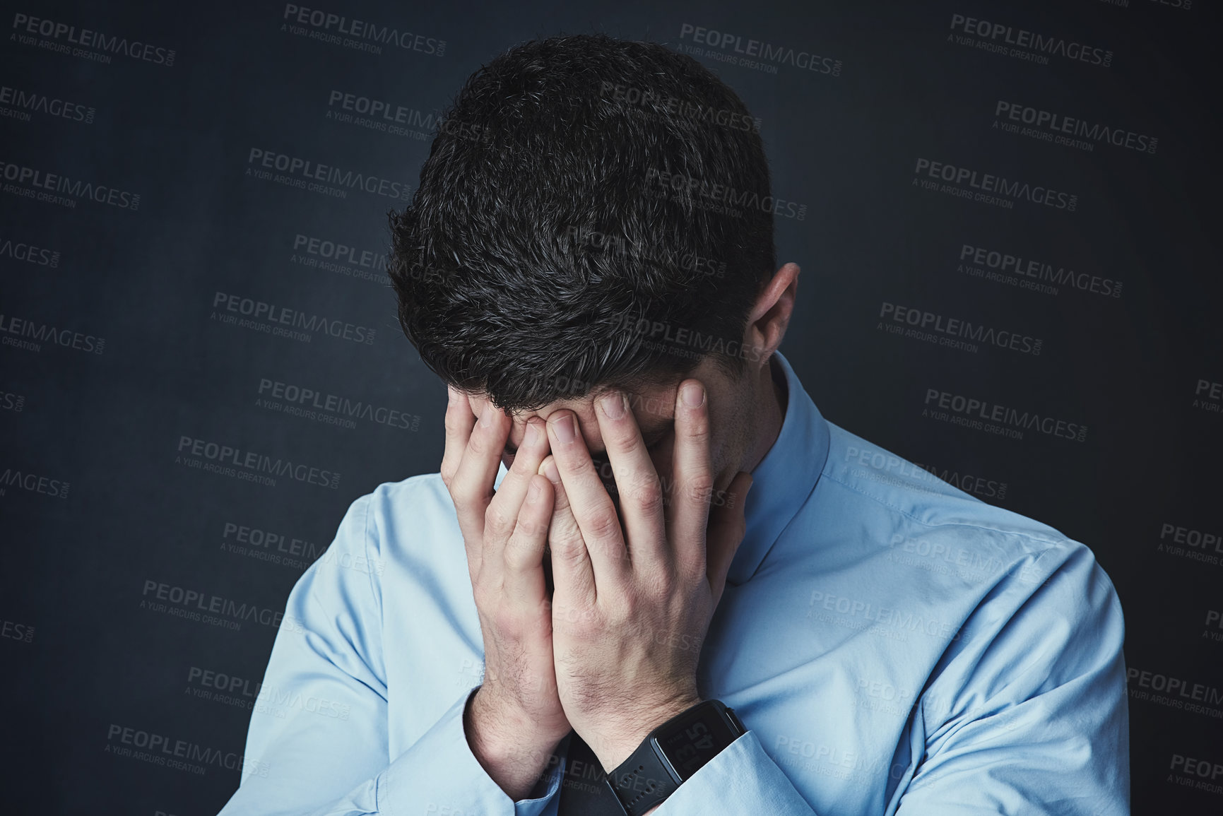 Buy stock photo Studio shot of a young businessman with his hands covering his face against a dark background