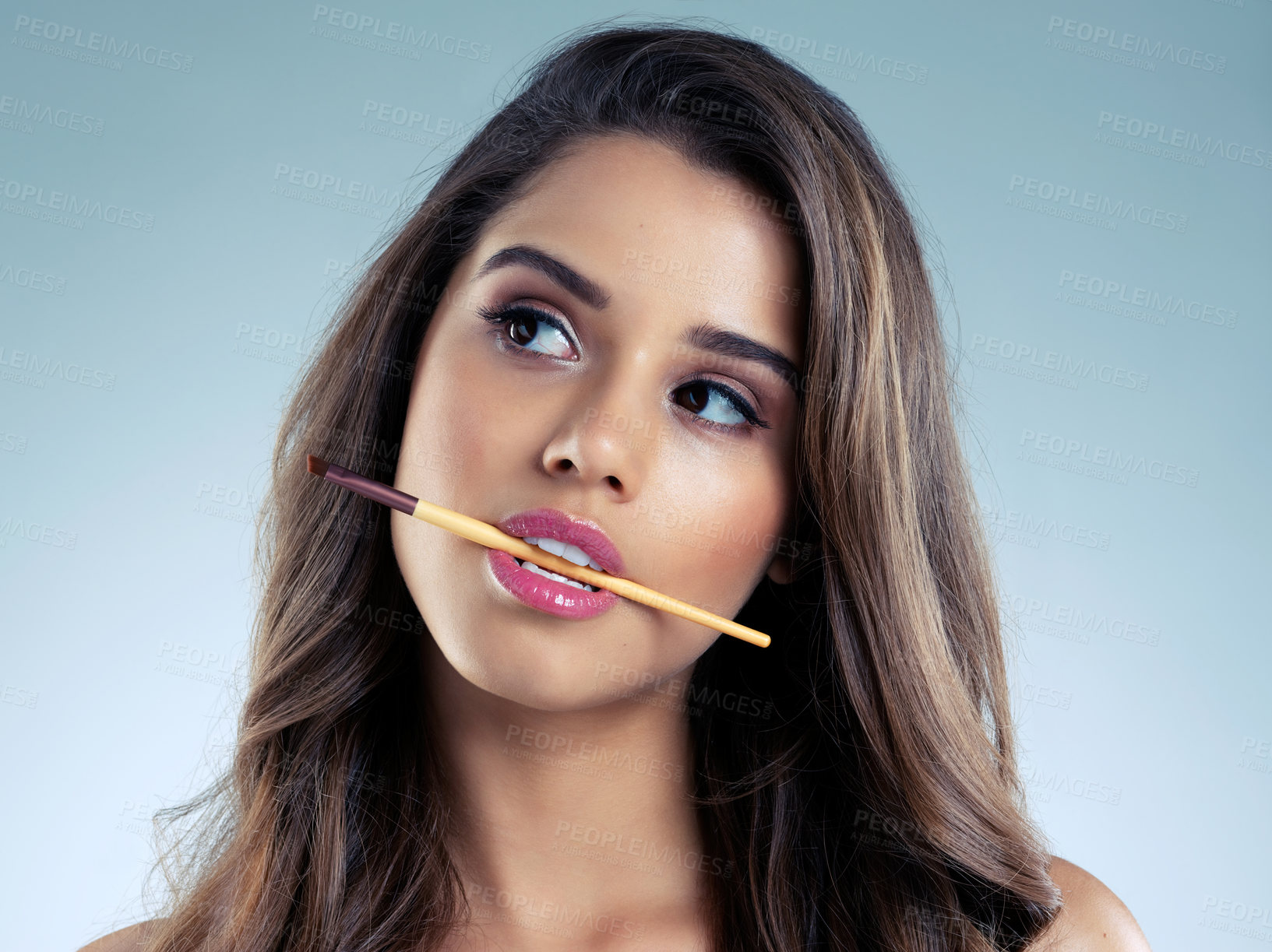 Buy stock photo Studio, thinking and woman with brush for makeup, eyeshadow and facial beauty with thoughts. Female model, cosmetics and tool in mouth for aesthetics, self care and foundation by blue background