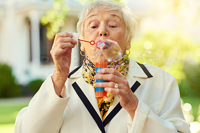 Buy stock photo Shot of a fun-loving senior woman blowing bubbles outside on a sunny day