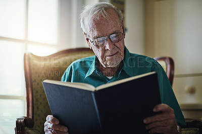 Buy stock photo Cropped shot of a senior man reading a book while relaxing at home
