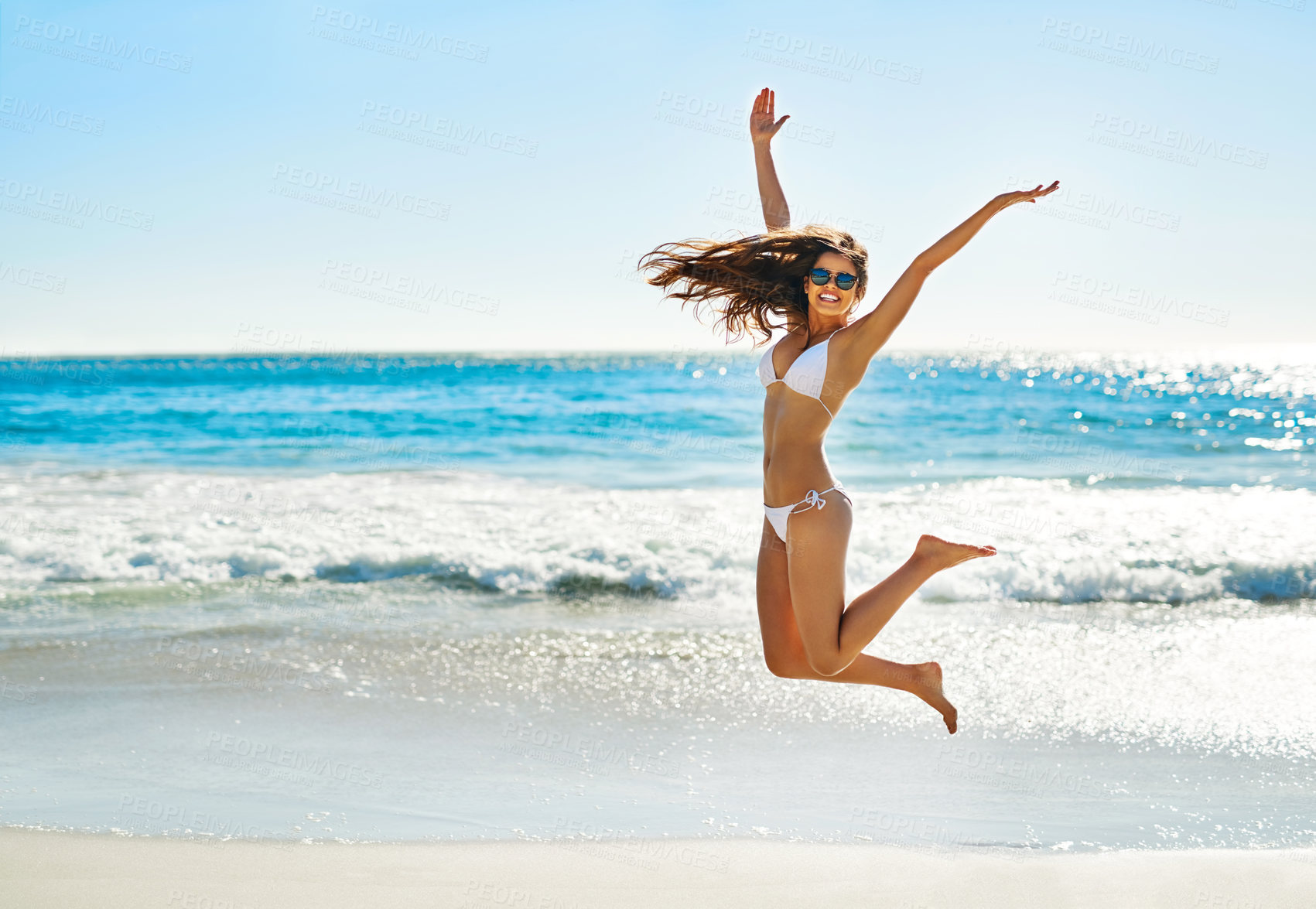 Buy stock photo Shot of a young woman jumping into mid air on the beach