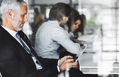 Buy stock photo Shot of a businessman using his digital tablet while sitting in a boardroom meeting