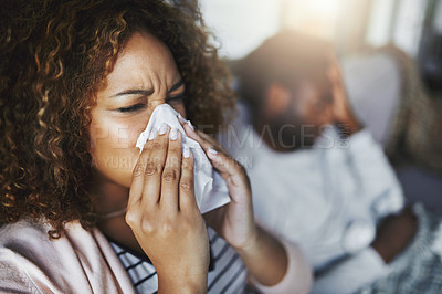 Buy stock photo Shot of a young woman blowing her nose with her boyfriend in the background