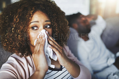 Buy stock photo Cropped shot of a young woman blowing her nose while sitting on the sofa