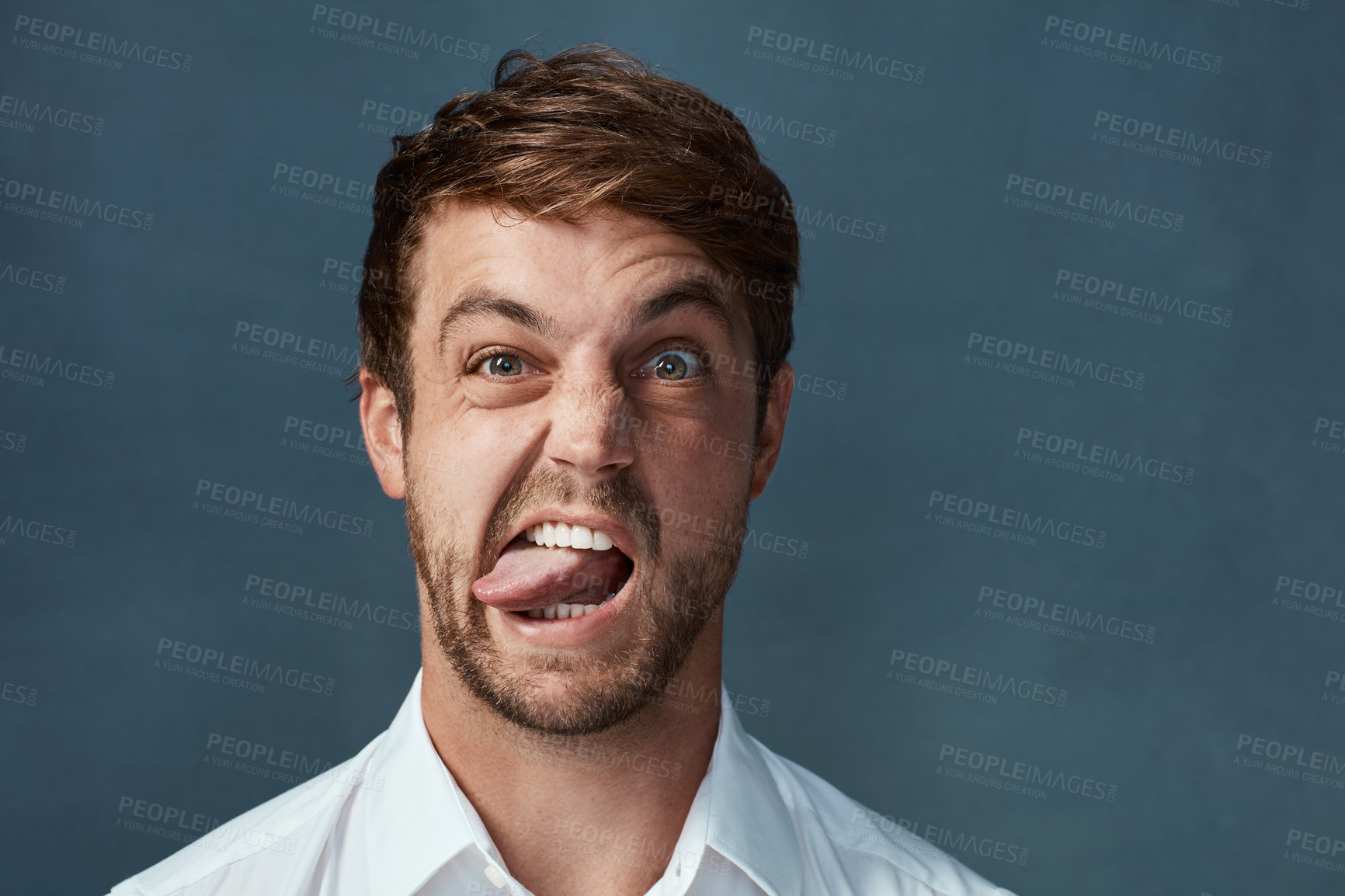 Buy stock photo Studio portrait of a handsome young man sticking his tongue out against a dark background