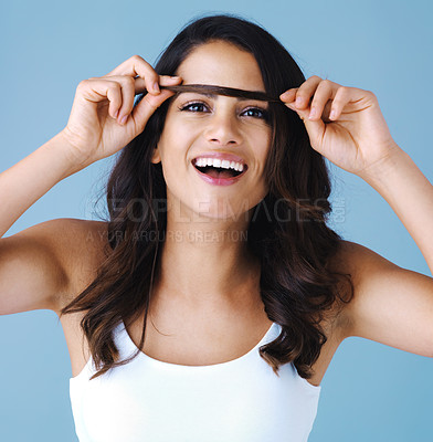 Buy stock photo Studio shot of an attractive young woman playing with her hair against a blue background