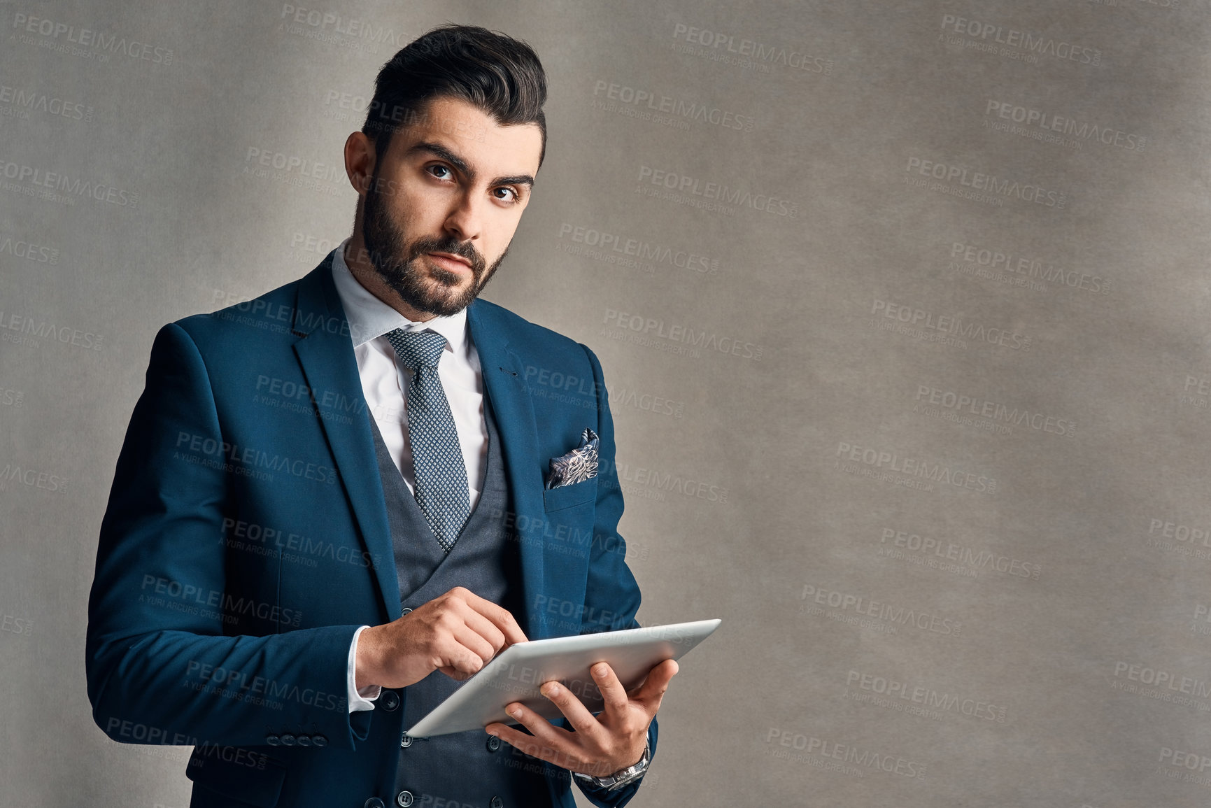Buy stock photo Studio portrait of a stylishly dressed young businessman using a digital tablet against a grey background