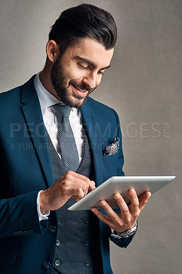 Buy stock photo Studio shot of a stylishly dressed young businessman using a digital tablet against a grey background
