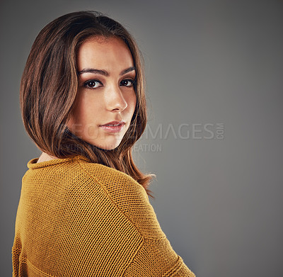 Buy stock photo Portrait of one trendy caucasian woman standing isolated against a grey studio background with copyspace. Beautiful young brunette female with attitude and style turning around to look at the camera