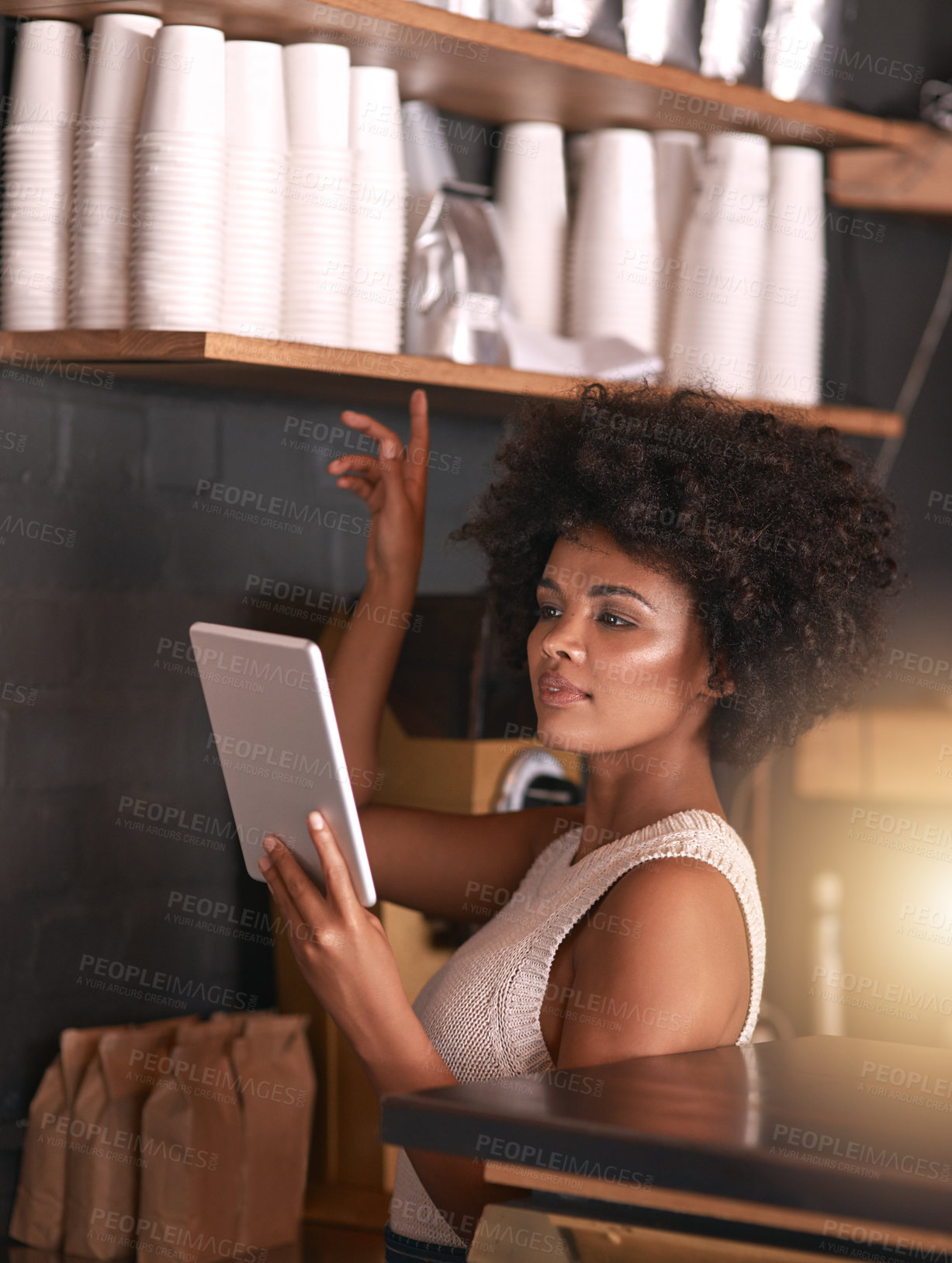 Buy stock photo Shot of a happy young business owner using her tablet while standing inside her coffee shop