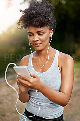 Buy stock photo Shot of a young woman listening to music on her phone while out for a run