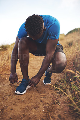 Buy stock photo Shot of a sporty young man tying his shoelaces before a run outside