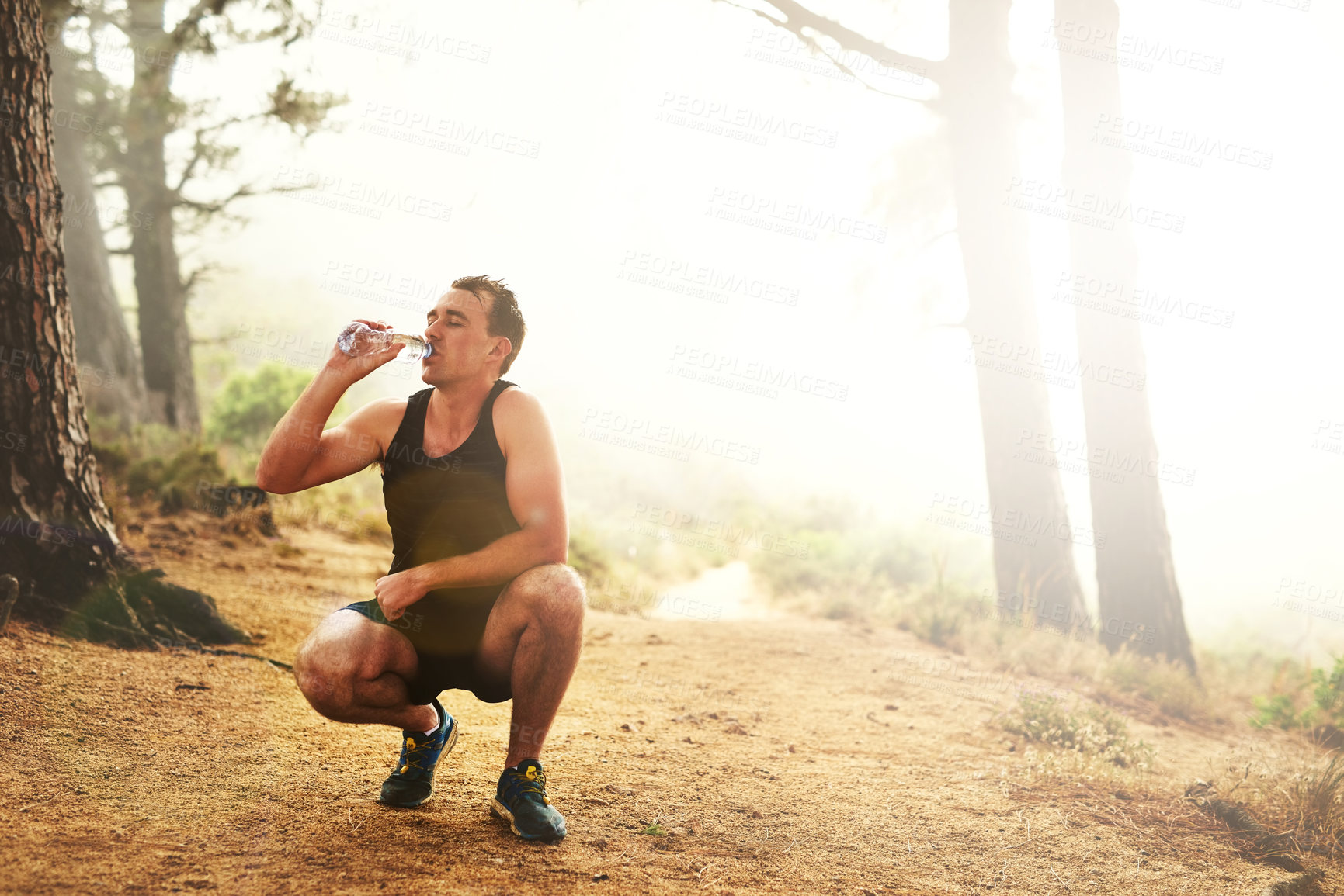 Buy stock photo Shot of a sporty young man drinking water while out for a run in the forest