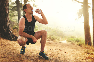 Buy stock photo Shot of a sporty young man drinking water while out for a run in the forest