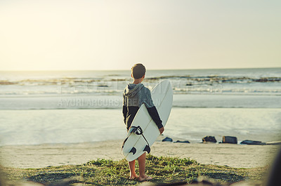 Buy stock photo Rearview shot of a young boy holding his surfboard while standing on the beach