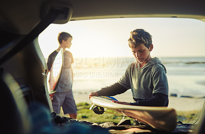 Buy stock photo Shot of two young brothers unloading their surfboards from the back of a car by the beach