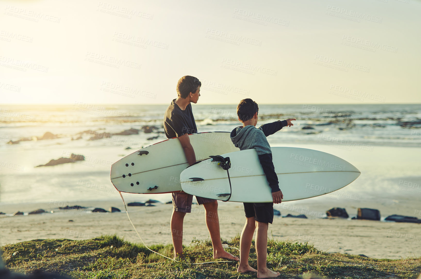 Buy stock photo Shot of two young brothers holding their surfboards while looking towards the ocean