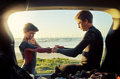 Buy stock photo Shot of a young surfer helping his little brother put on his wetsuit at the beach