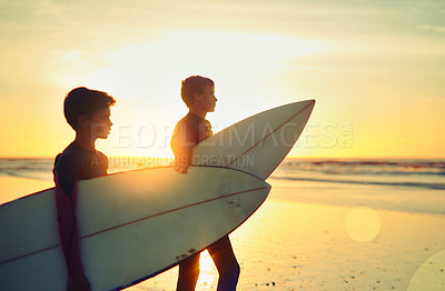 Buy stock photo Shot of two young brothers holding their surfboards while looking towards the ocean