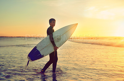 Buy stock photo Shot of a young surfer walking into the water with his surfboard under his arm