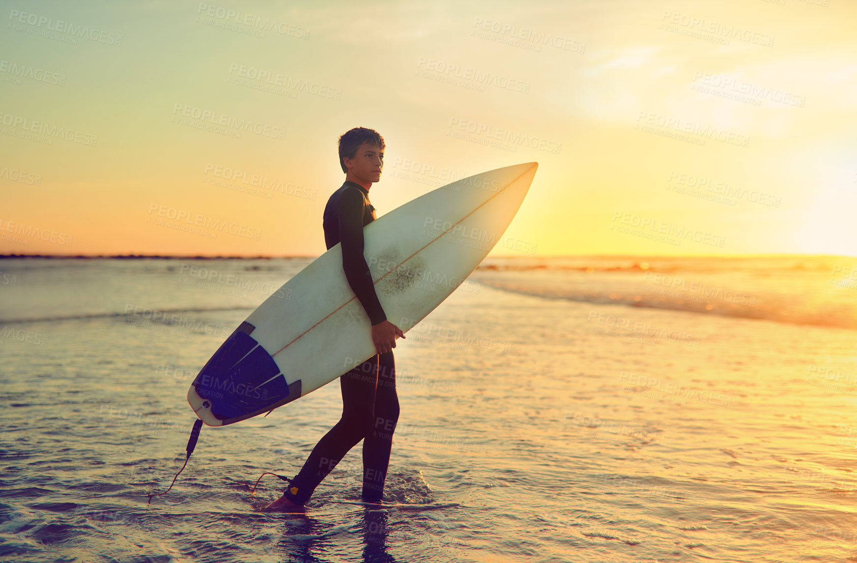 Buy stock photo Shot of a young surfer walking into the water with his surfboard under his arm