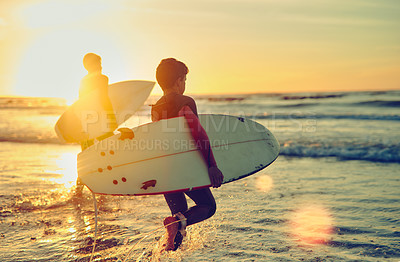 Buy stock photo Shot of two young brothers carrying their surfboards while wading into the ocean