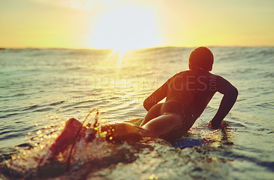 Buy stock photo Rearview shot of a young surfer paddling up a swell on his surfboard