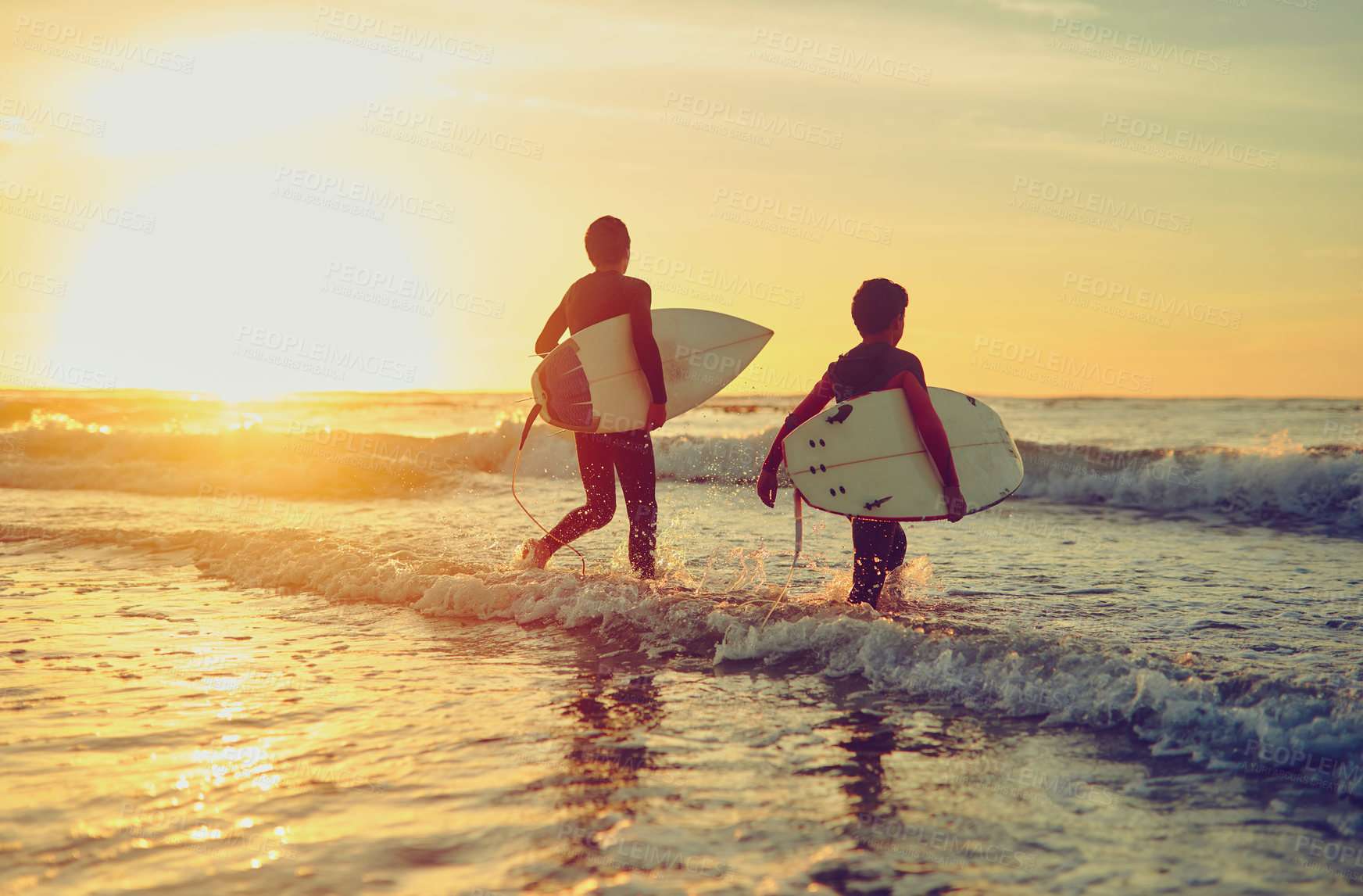 Buy stock photo Shot of two young brothers carrying their surfboards while wading into the ocean