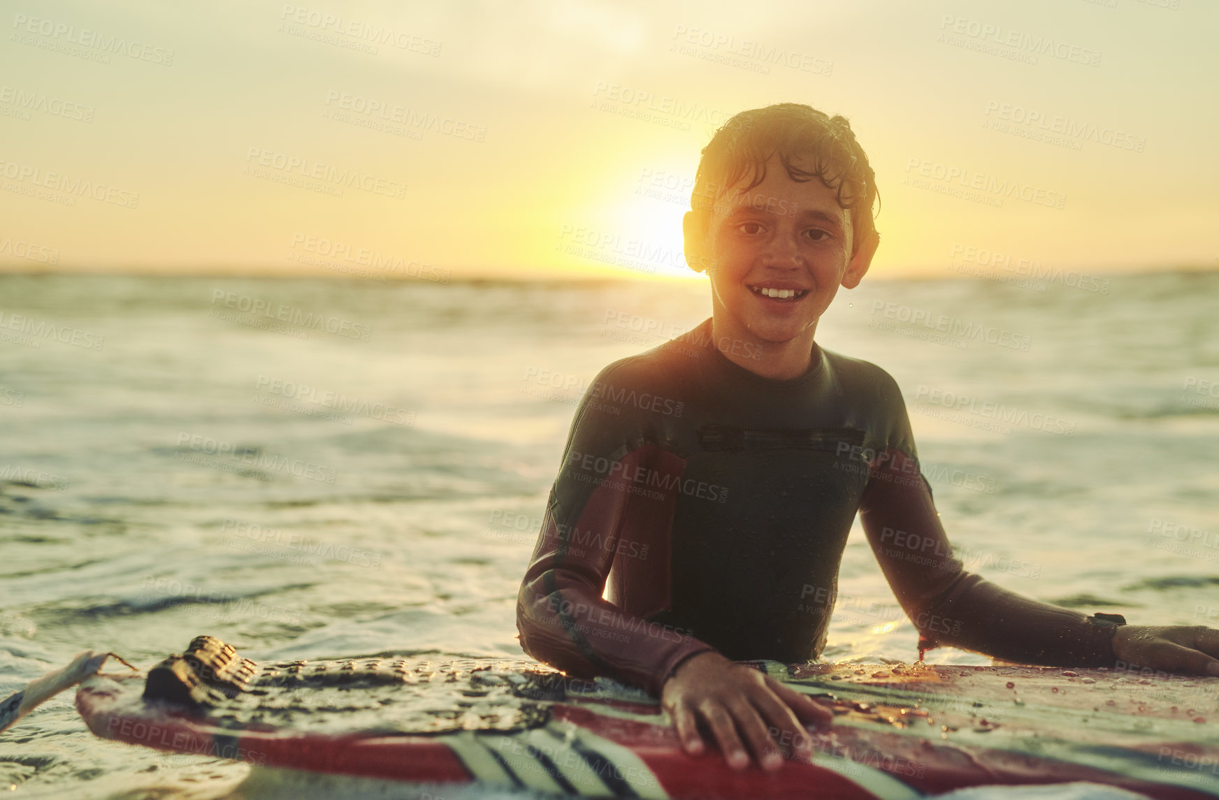 Buy stock photo Portrait of a young boy in a wetsuit sitting on his surfboard in the ocean