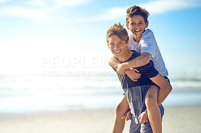 Buy stock photo Portrait of a happy young boy giving his little brother a piggyback ride on the beach