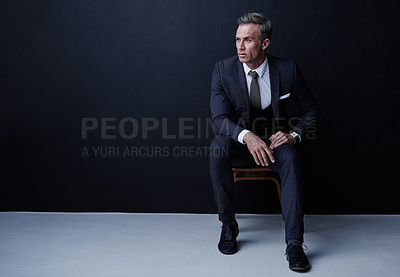 Buy stock photo Studio shot of a mature businessman sitting on a chair against a dark background