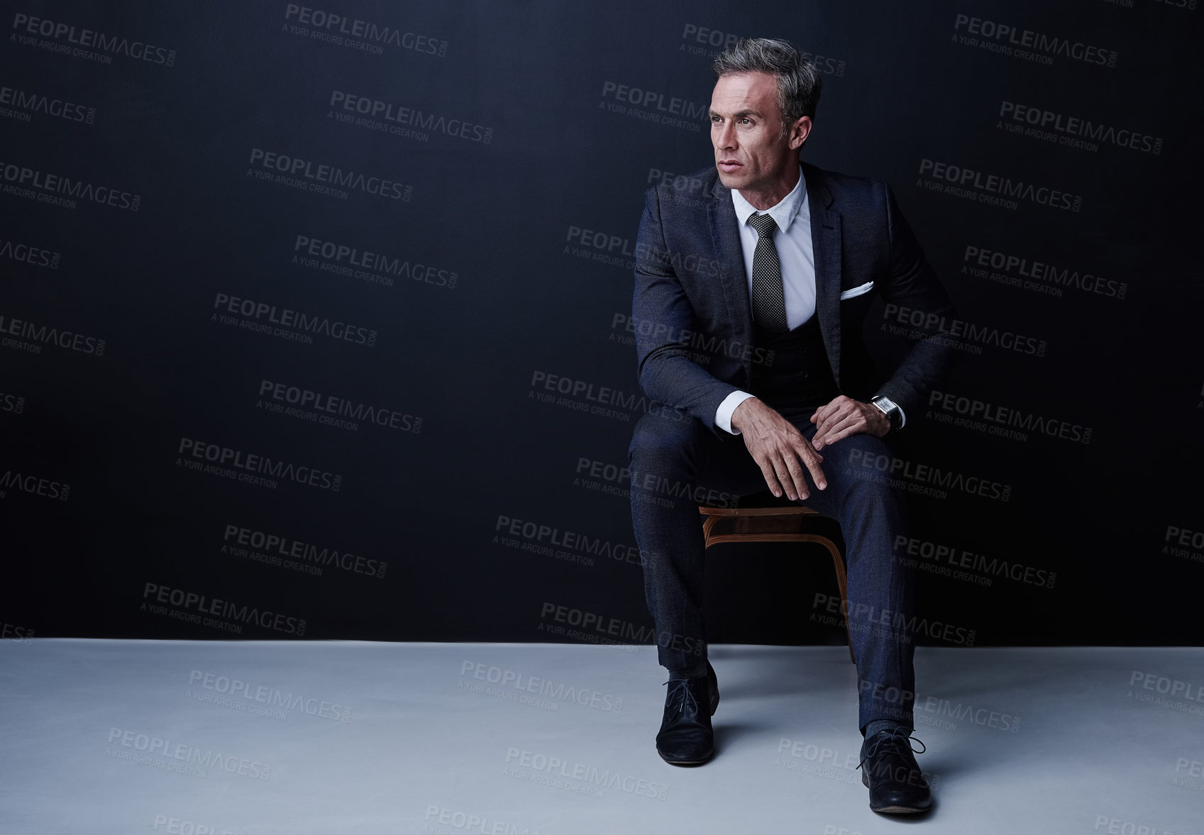 Buy stock photo Studio shot of a mature businessman sitting on a chair against a dark background