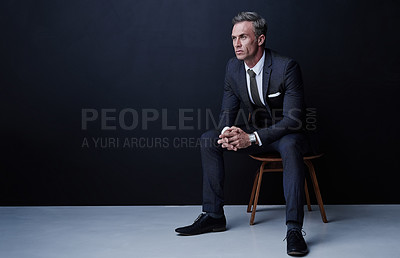 Buy stock photo Studio shot of a mature businessman sitting on a chair against a dark background