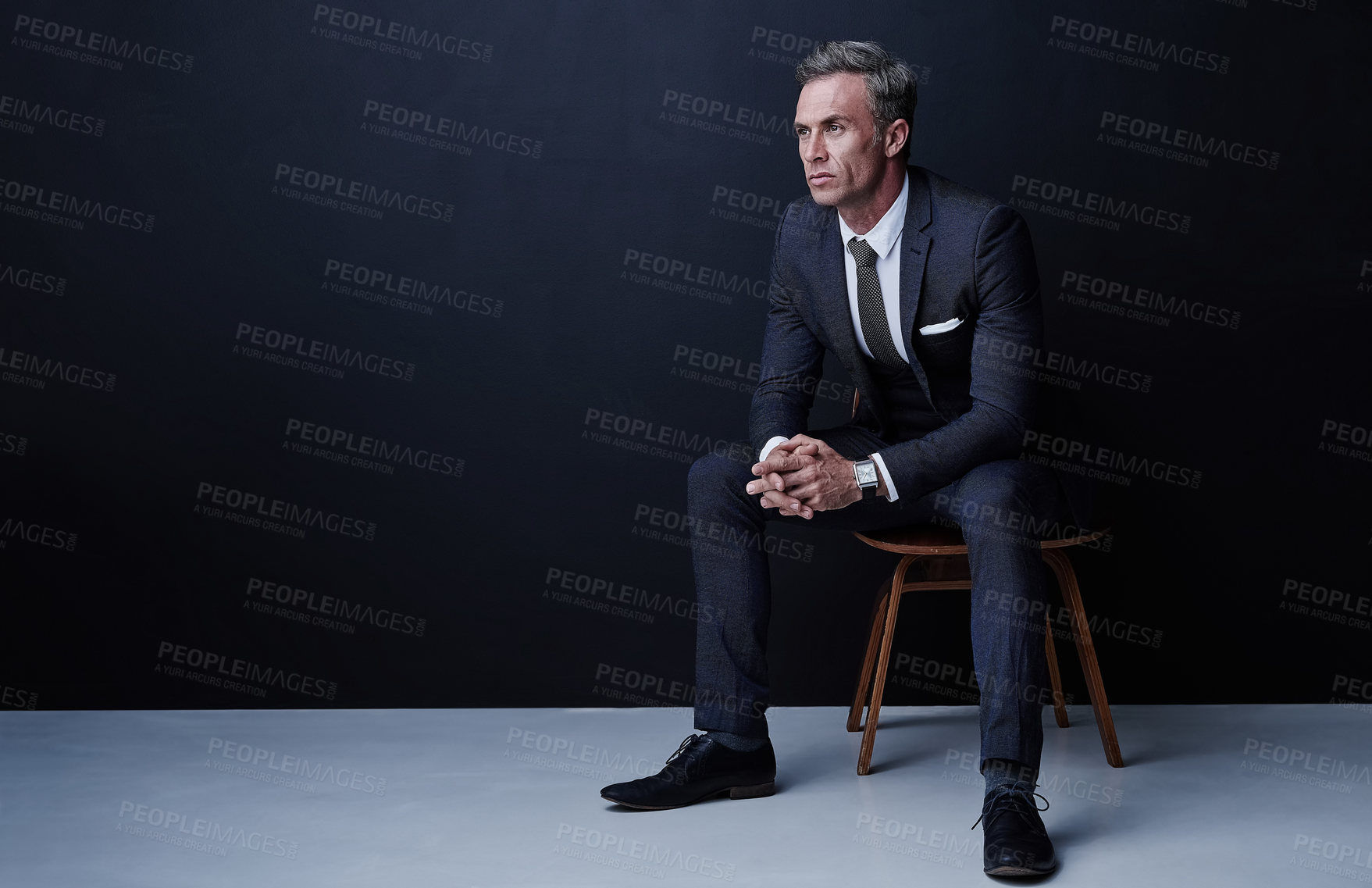 Buy stock photo Studio shot of a mature businessman sitting on a chair against a dark background