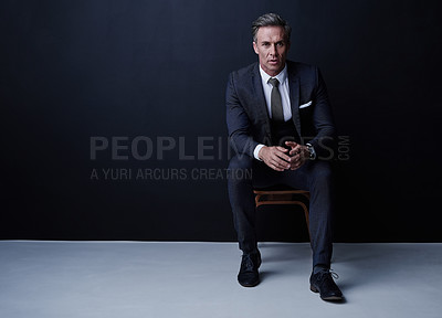 Buy stock photo Studio portrait of a mature businessman sitting on a chair against a dark background