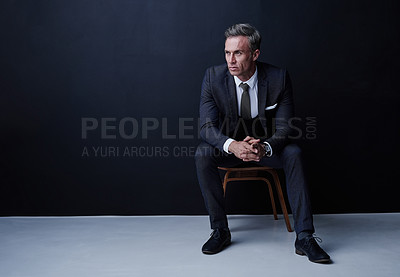 Buy stock photo Studio shot of a mature businessman sitting on a chair against a dark background