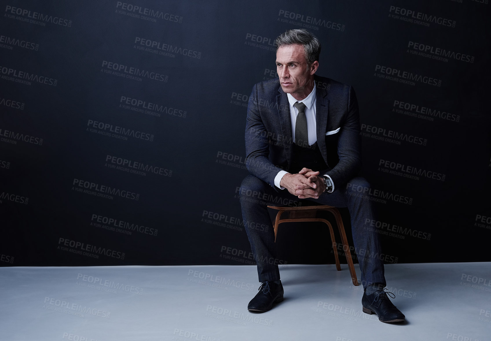 Buy stock photo Studio shot of a mature businessman sitting on a chair against a dark background