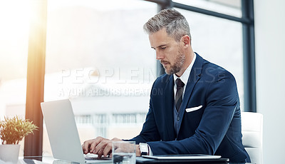 Buy stock photo Shot of a corporate businessman working on a laptop in an office