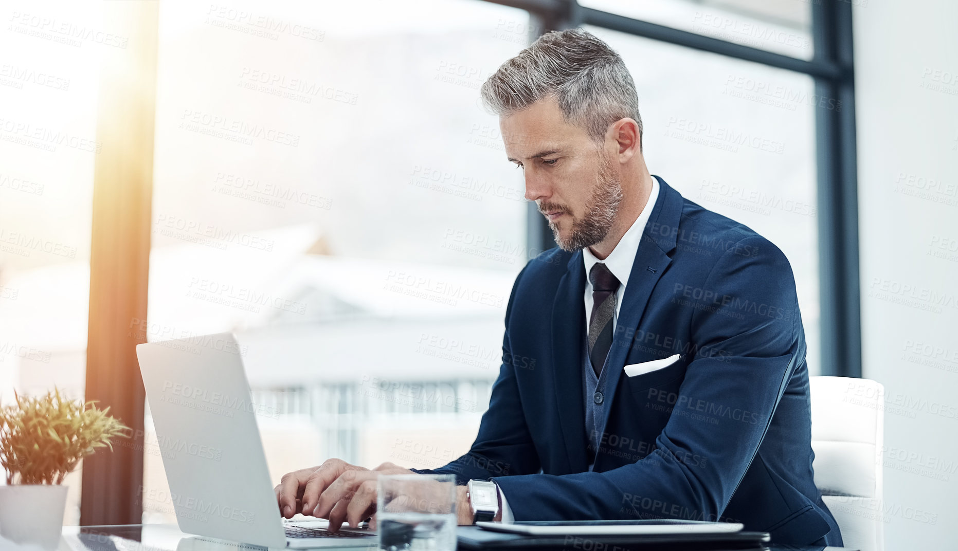 Buy stock photo Shot of a corporate businessman working on a laptop in an office