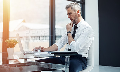 Buy stock photo Shot of a corporate businessman working on a laptop in an office